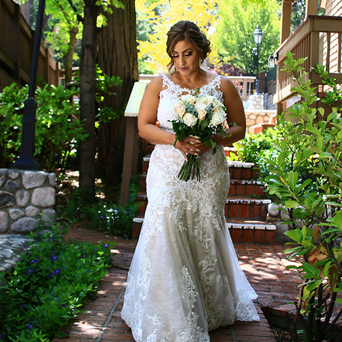 A woman in white dress holding flowers near stairs.