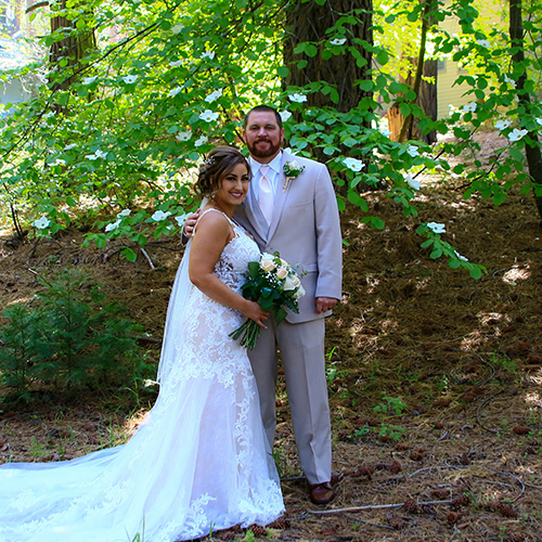 A bride and groom pose for a picture in the woods.