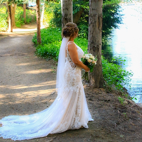 A bride in her wedding dress standing by the water.